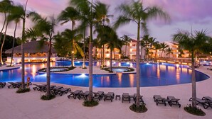A resort pool area with multiple swimming pools, palm trees, and lounge chairs.