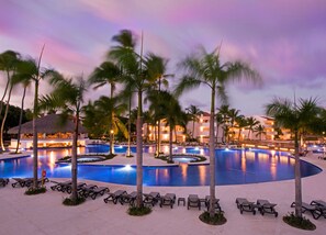 A resort pool area with multiple swimming pools, palm trees, and lounge chairs.