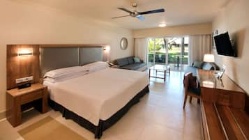 Habitación de hotel con una cama grande, un escritorio, una silla, un televisor y un balcón con mobiliario exterior.