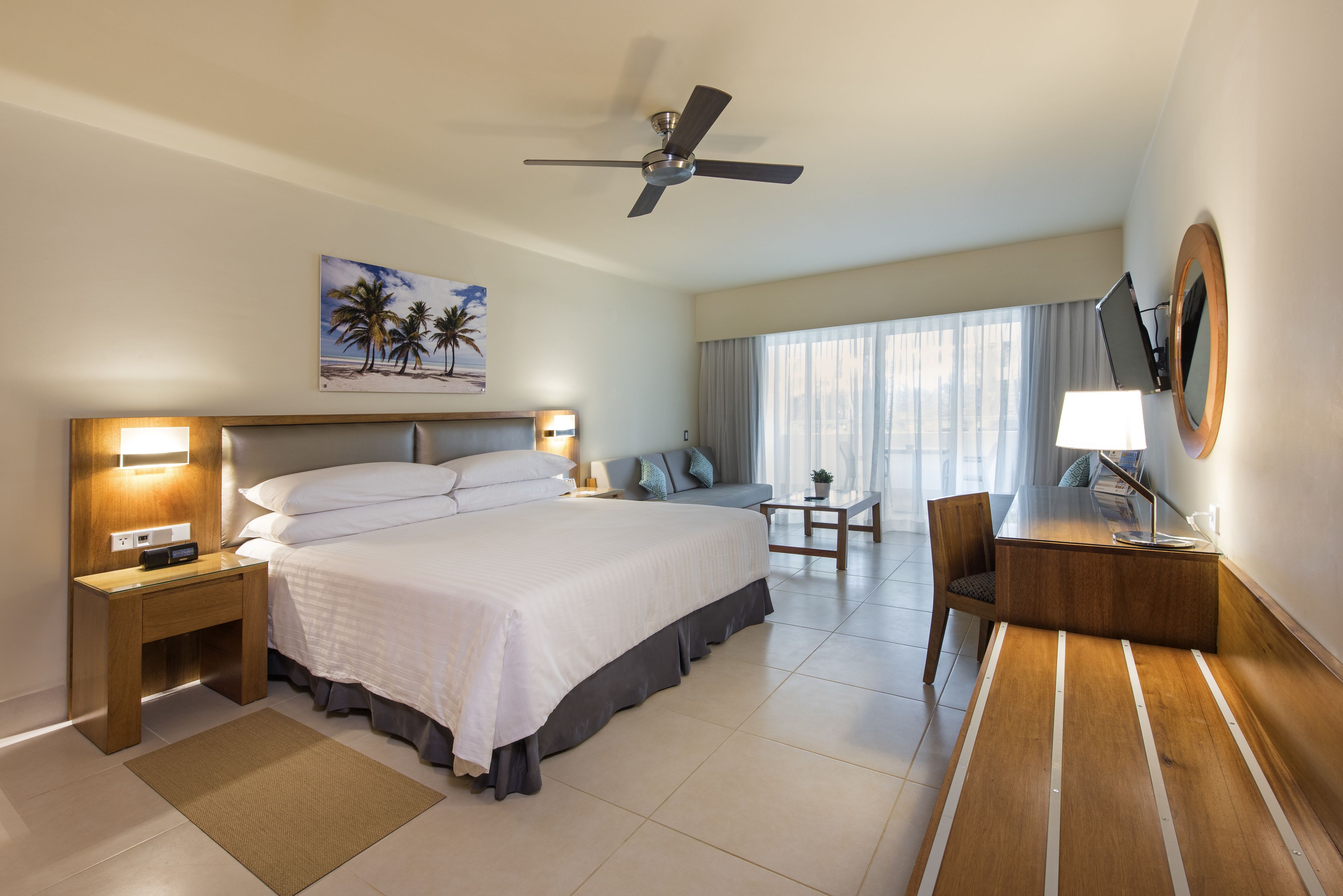 A hotel room with a bed, bedside table, lamp, desk, chair, TV, and a ceiling fan.