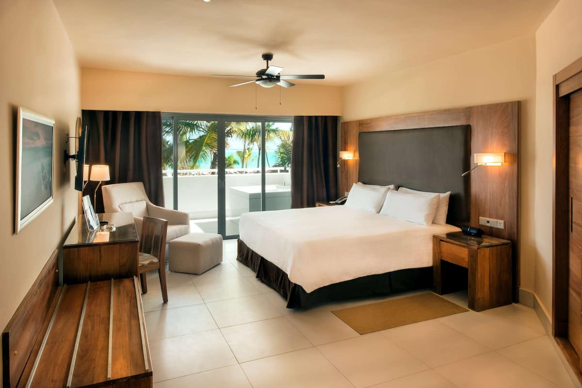 A hotel room with a bed, a desk, a chair, a ceiling fan, and a view of the outdoors.