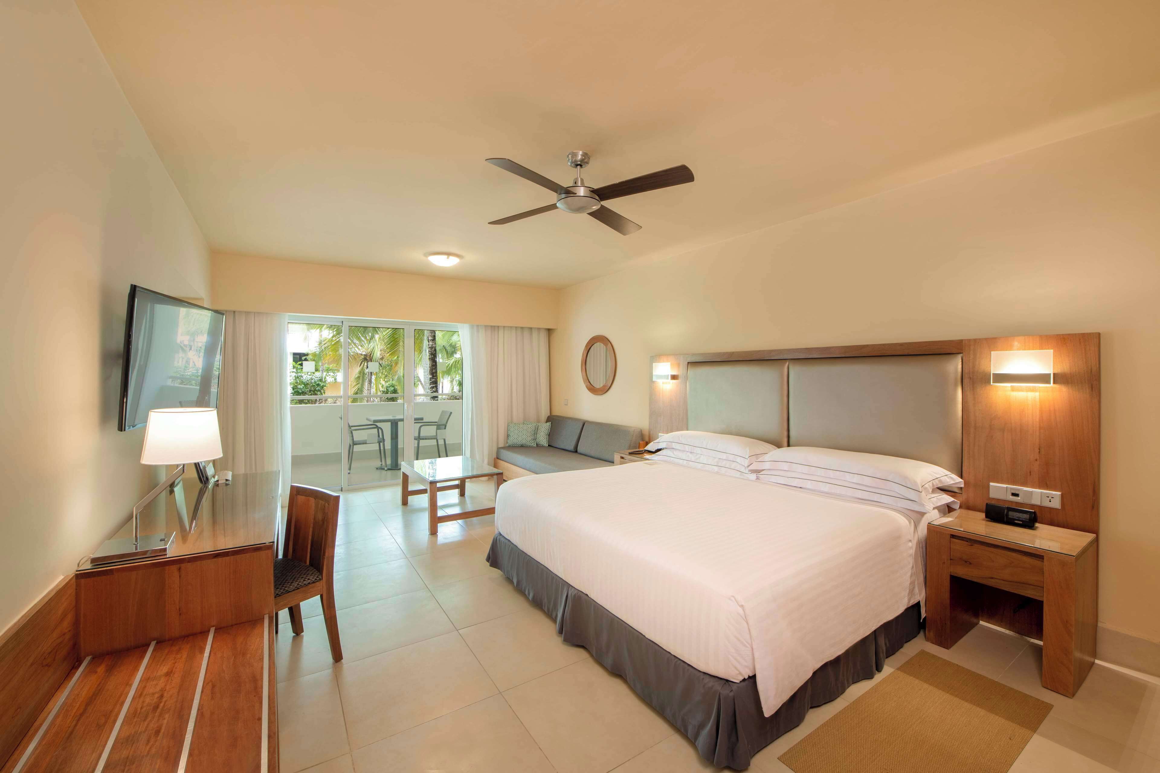 A hotel room with a bed, desk, chair, and a ceiling fan.