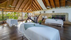 A spacious room with wooden flooring, two beds with white linens, a stone wall, and a ceiling fan. - Occidental Punta Cana - All Inclusive (Punta Cana)