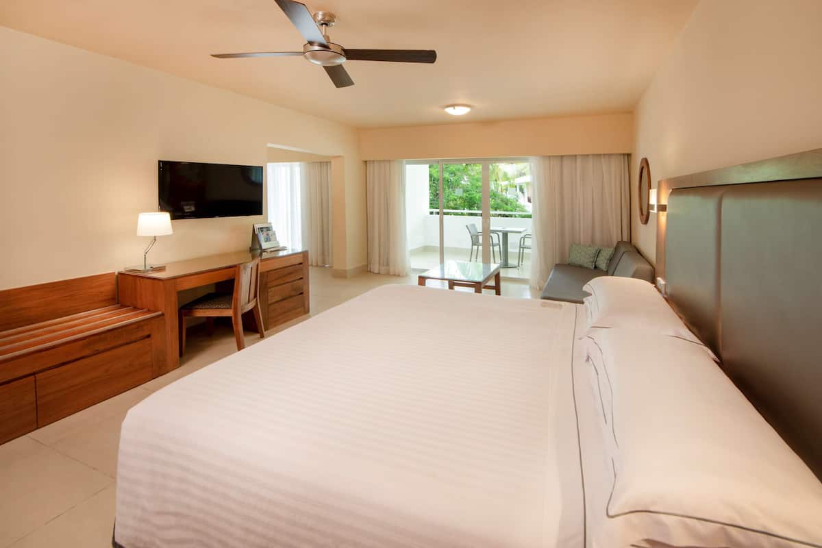 A hotel room with a large bed, a desk with a chair, a television, and a balcony with a table and chairs.