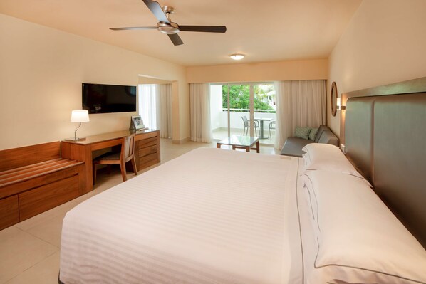 A hotel room with a large bed, a desk with a chair, a television, and a balcony with a table and chairs. - Occidental Punta Cana - All Inclusive (Punta Cana)