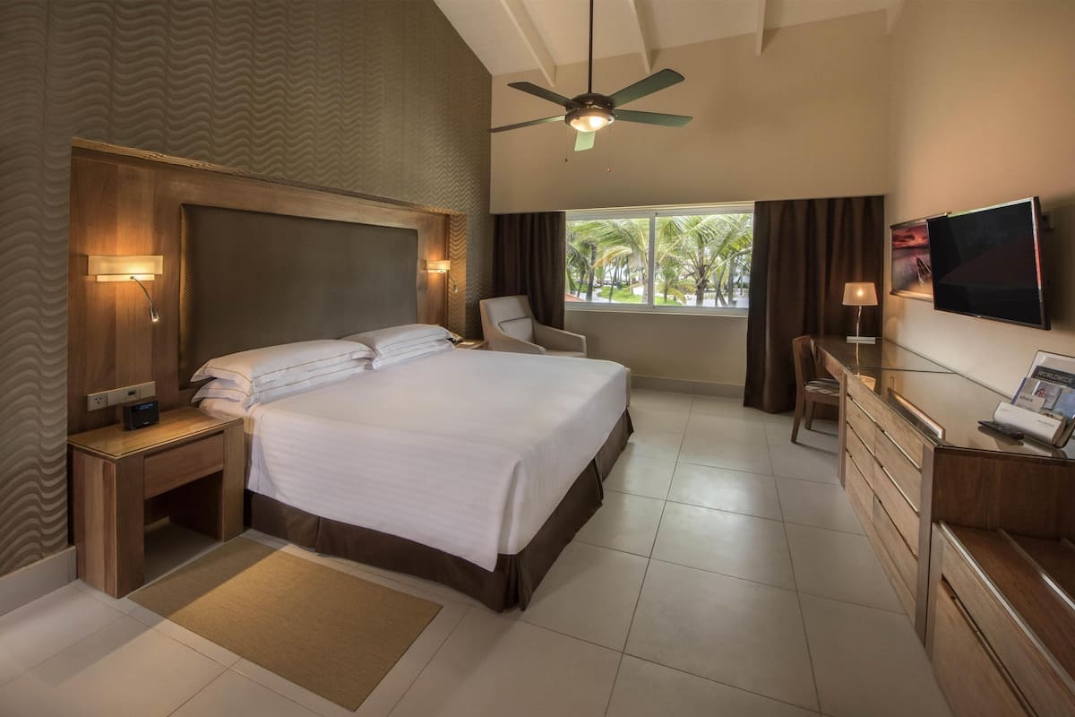 Une chambre d’hôtel avec un grand lit, un bureau, une chaise, une télévision et un ventilateur de plafond.