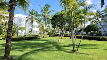 Un jardín bien cuidado con palmeras y césped impecable, rodeado de edificios blancos con balcones.