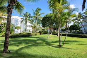 A well-maintained garden with palm trees and manicured lawns, surrounded by white buildings with balconies.