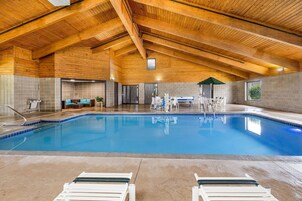 Piscina interior con techo de madera, sillones de descanso y zona de sauna.