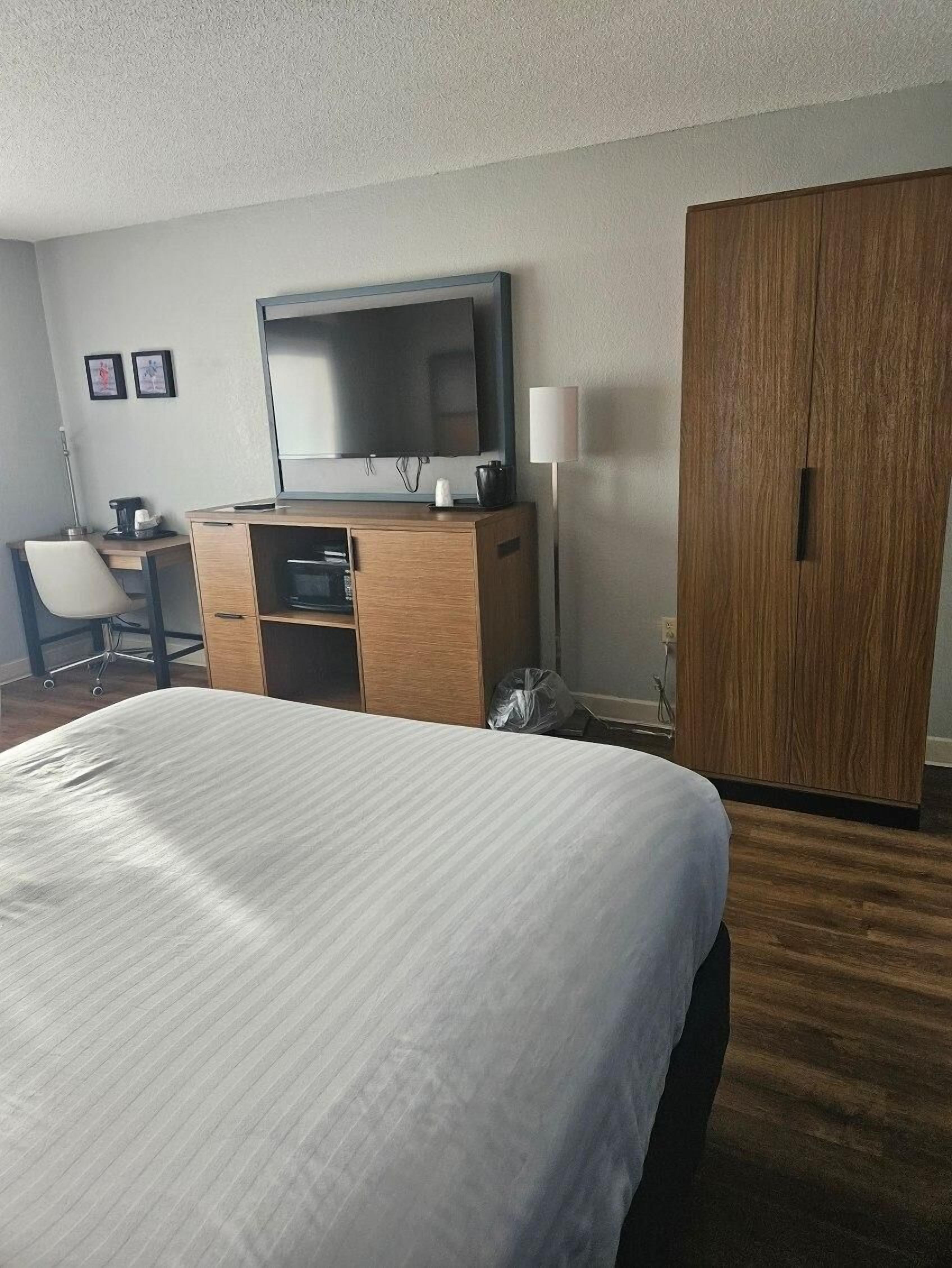 Ein Hotelzimmer mit Bett, Schreibtisch mit Stuhl, Fernseher, Kleiderschrank und Lampe.