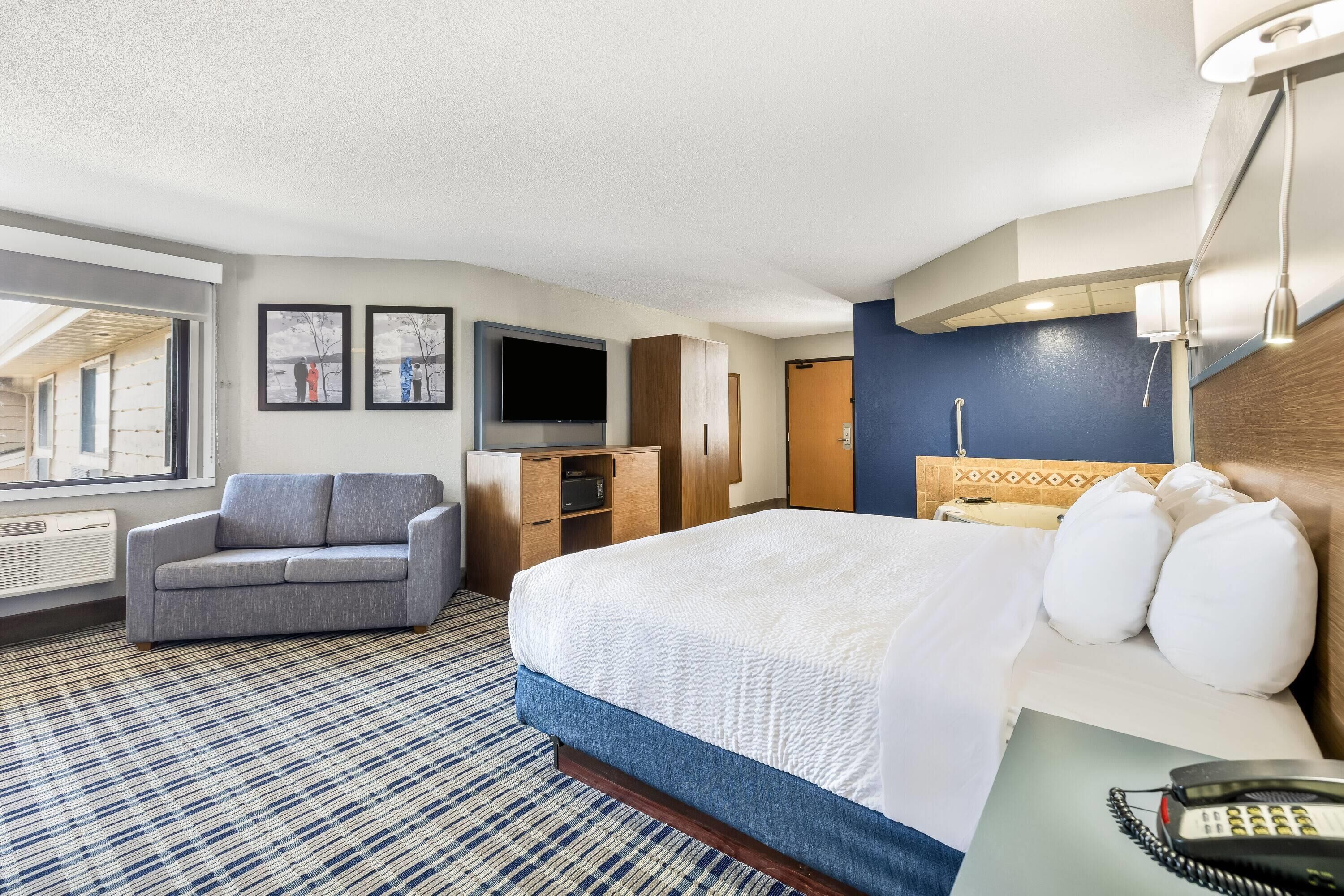A hotel room with a bed, a sofa, a television, a desk, and a window.