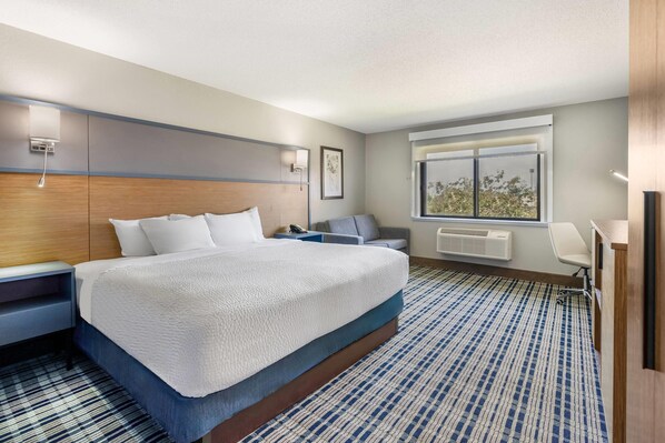 Habitación de hotel con una cama grande, un escritorio, una silla, un ventanal y un radiador.