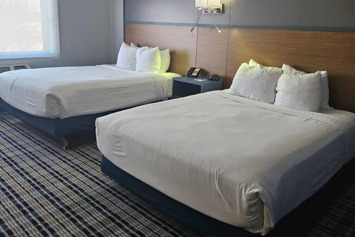 A hotel room with two beds, a nightstand with a phone, and a wall-mounted light.