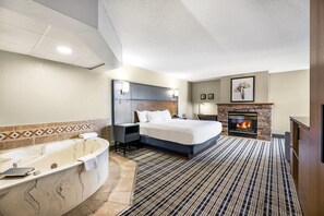 A hotel room with a large bed, a fireplace, a bathtub, and a striped carpet. - AmericInn by Wyndham Albert Lea (Albert Lea)