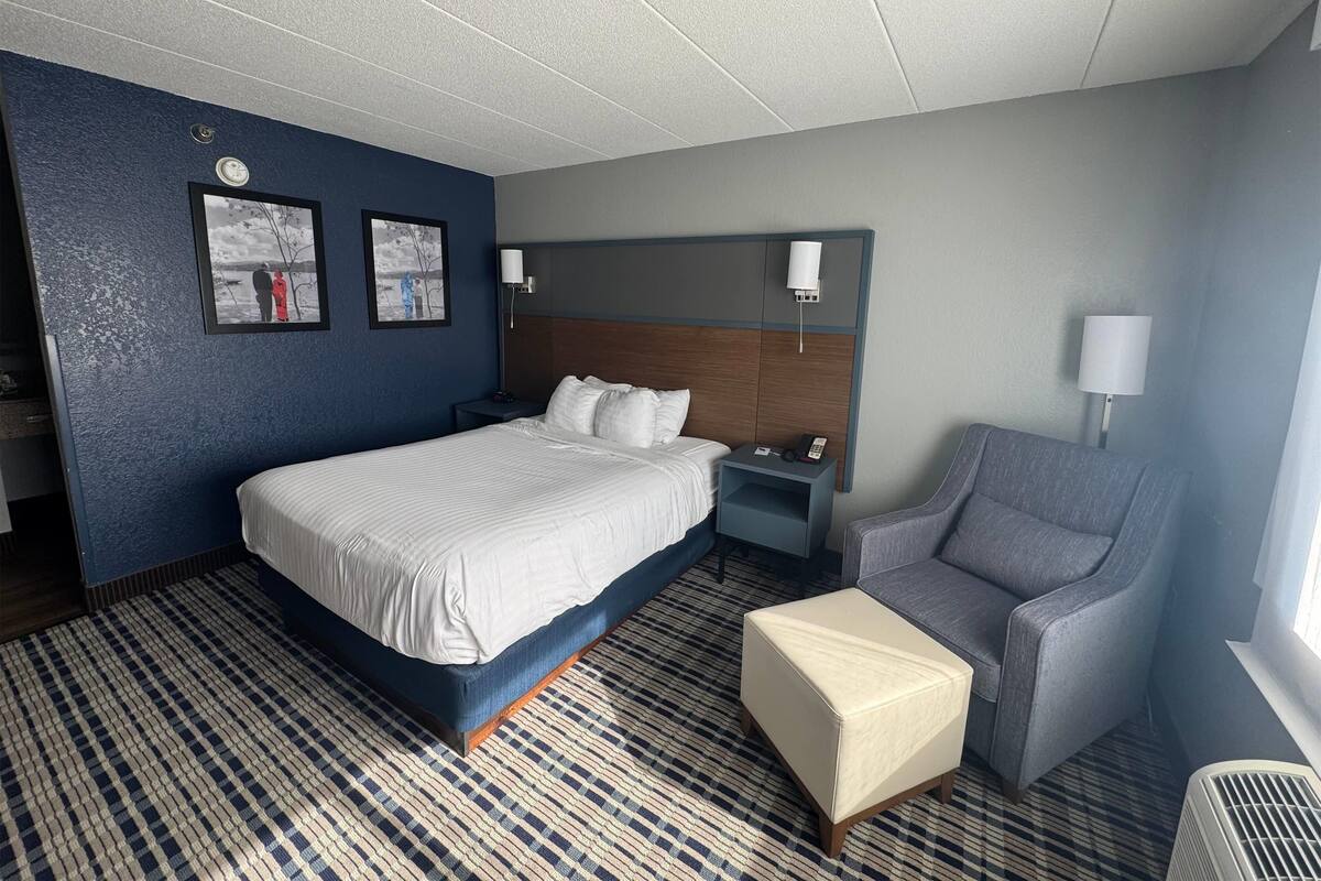 A hotel room with a large bed, a bedside table, a chair, and a small table.