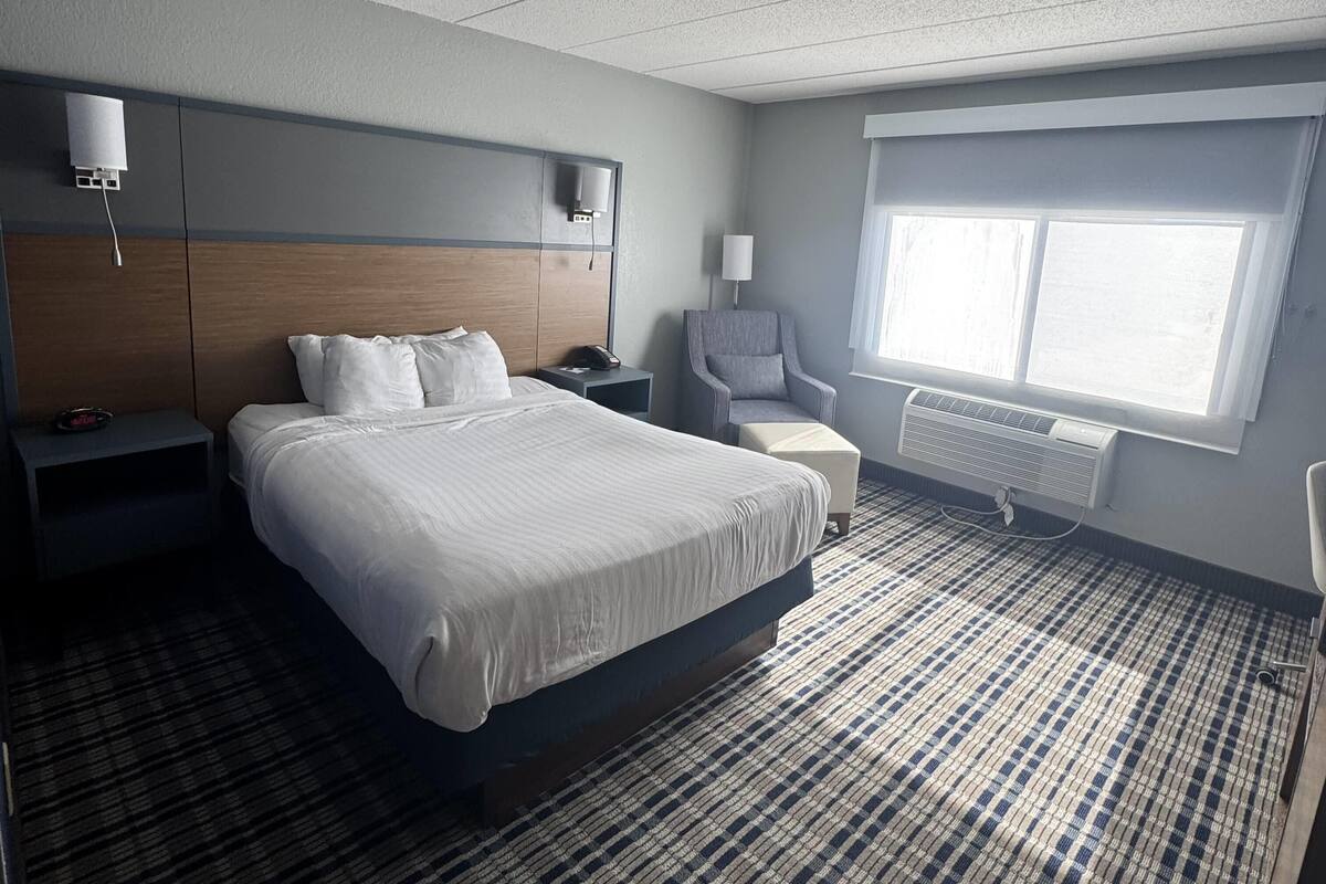A hotel room with a large bed, bedside tables, a chair, a desk, a TV, and a window with a view.