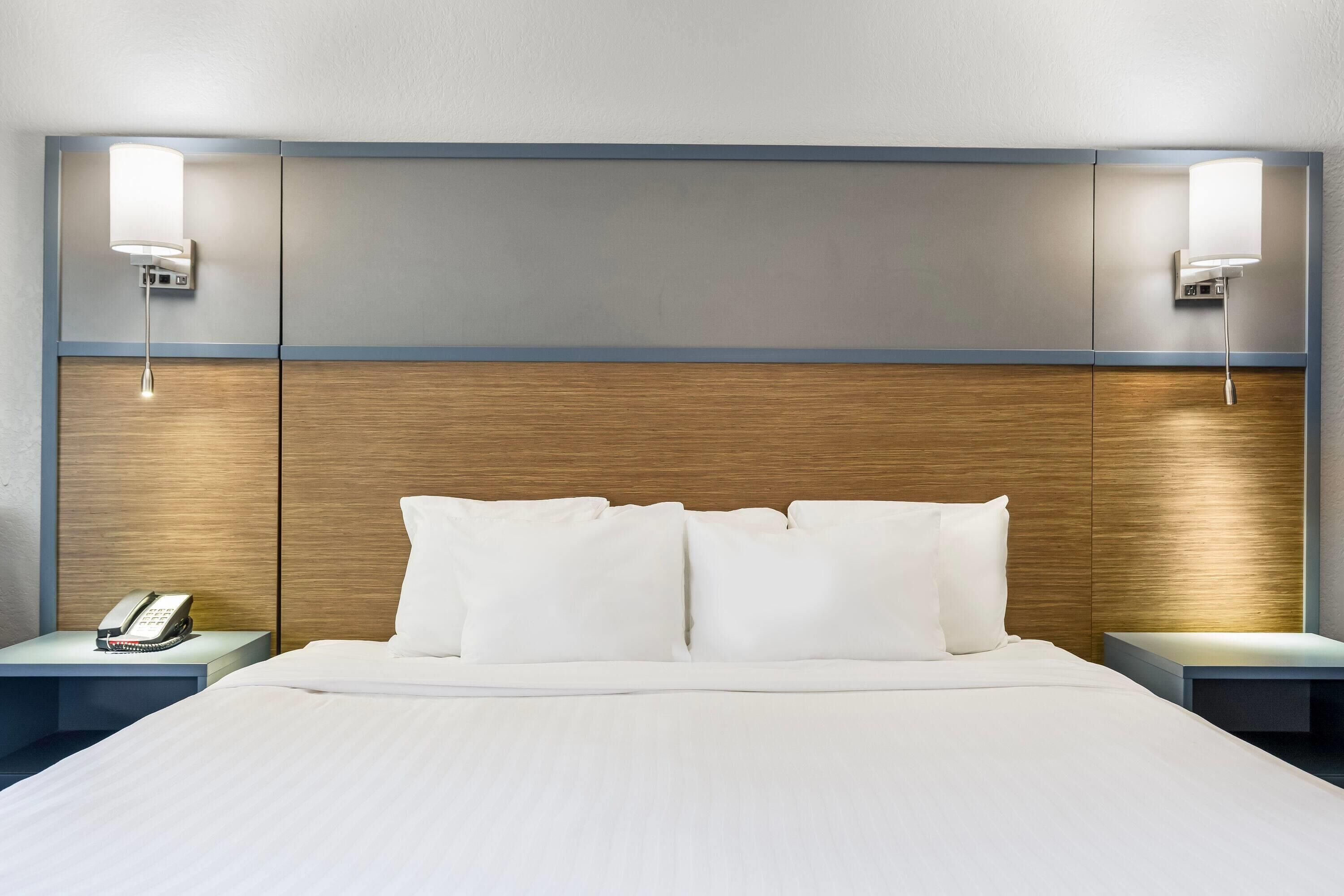 Une chambre d’hôtel avec un grand lit, deux tables de chevet, un téléphone et des lampes fixées au mur.