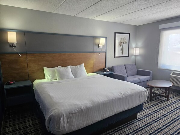 A hotel room with a large bed, a grey sofa, a small round table, and a framed picture on the wall. - AmericInn by Wyndham Albert Lea (Albert Lea)