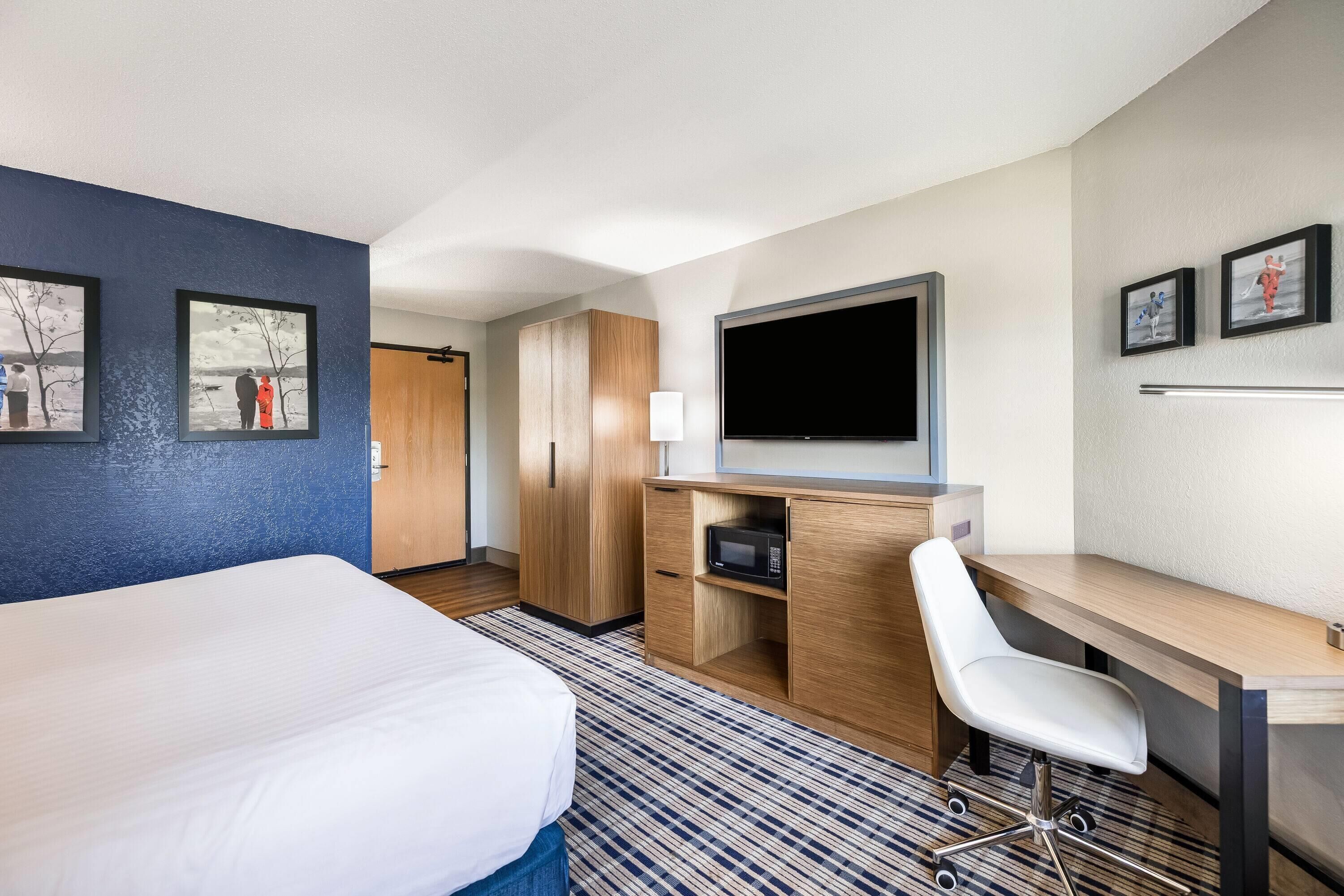 Una habitación de hotel con cama, escritorio con silla, televisión y obras de arte en las paredes.