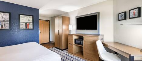 Una habitación de hotel con cama, escritorio con silla, televisión y obras de arte en las paredes.