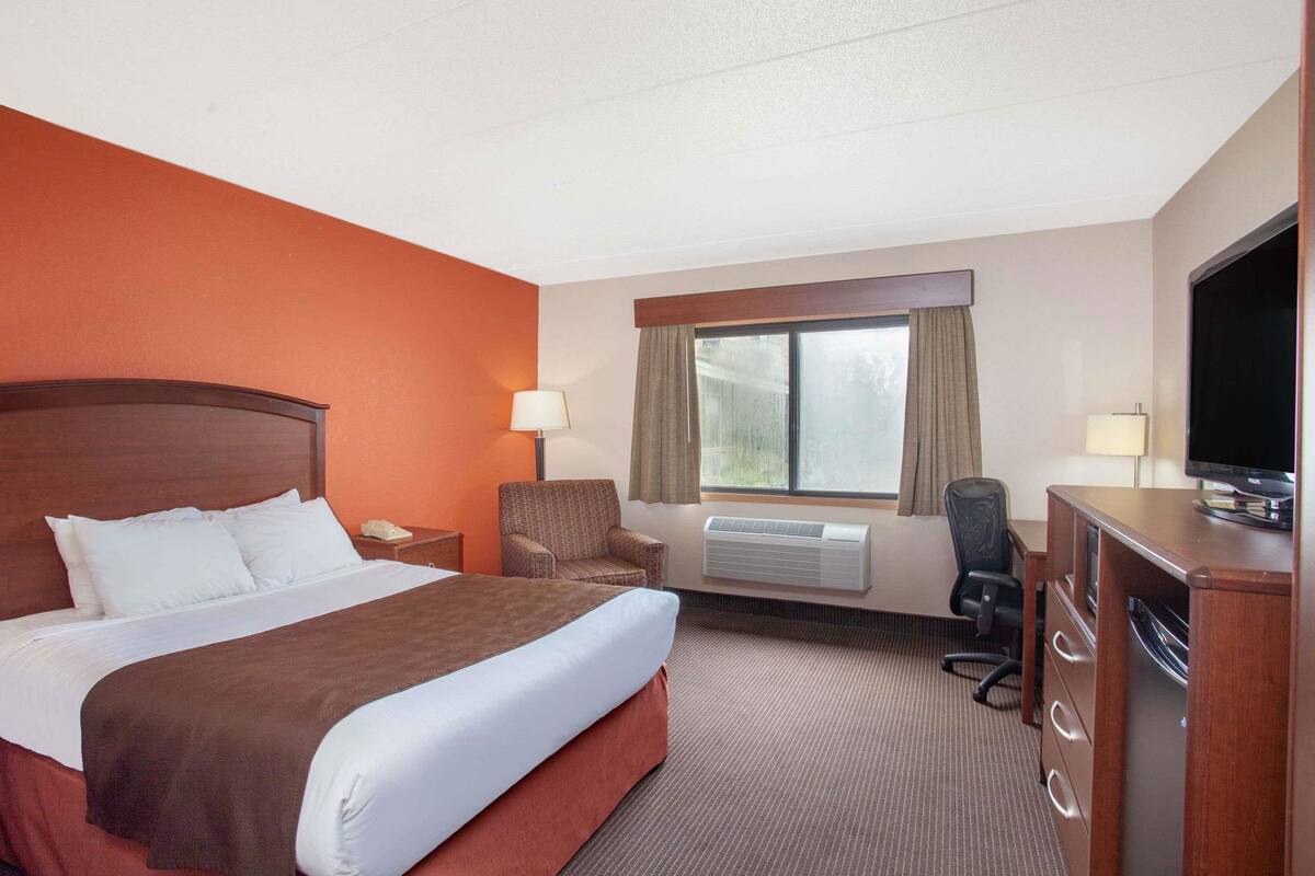 A hotel room with a bed, a desk, a chair, a television, and an air conditioning unit.
