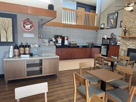 Interior de una cafetería con mostrador, zona de estar y pared de ladrillo.