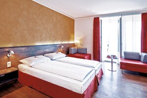 A hotel room with two beds, a sofa, a small table, and a view of the outside.
