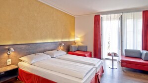 Et hotelværelse med en stor seng, en rød sofa, et lille bord og udsigt til det fri.