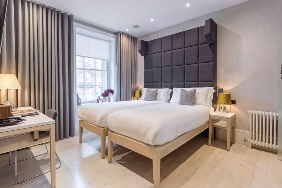 A modern hotel room with a large bed, bedside tables, a desk, and a window with curtains.
