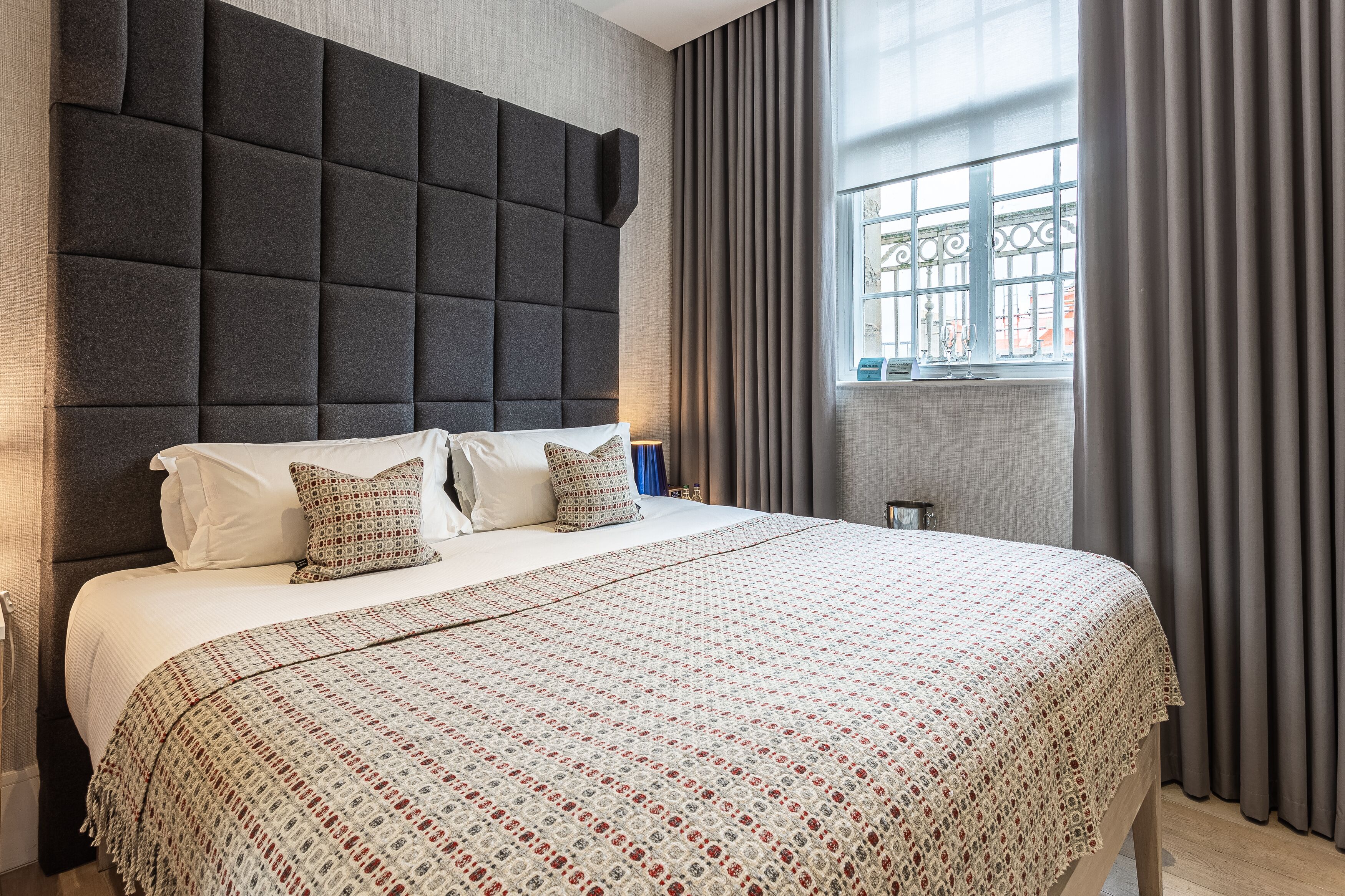 A hotel room with a large bed, a dark headboard, and a window with curtains.