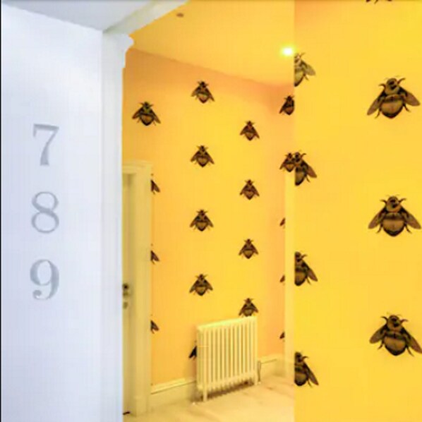 A hallway with a yellow wall featuring a pattern of bee images. A white door with the numbers 789 is visible on the left.