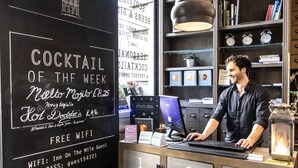 Un coin bar avec un menu écrit à la craie, un homme qui travaille sur un ordinateur et une lampe de style rétro.