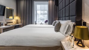 Une chambre d’hôtel avec un grand lit, un bureau avec une lampe, une télévision et une fenêtre avec des rideaux.