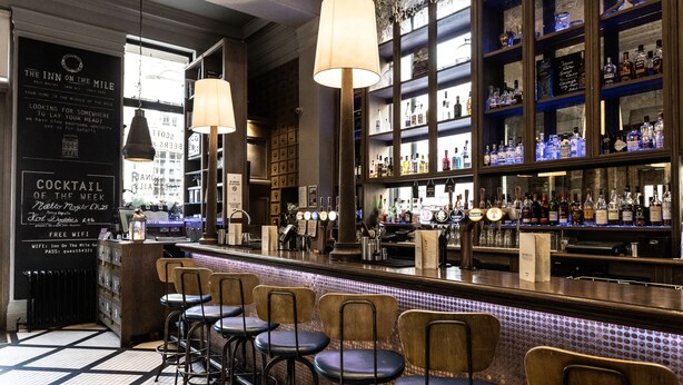 Un espace bar avec un sol carrelé, des tabourets de bar et une étagère bien garnie de bouteilles d’alcool.