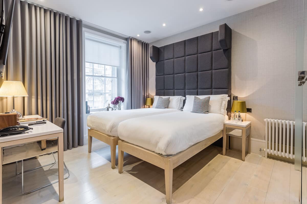 A modern hotel room with two beds, a desk, and a large window with curtains.