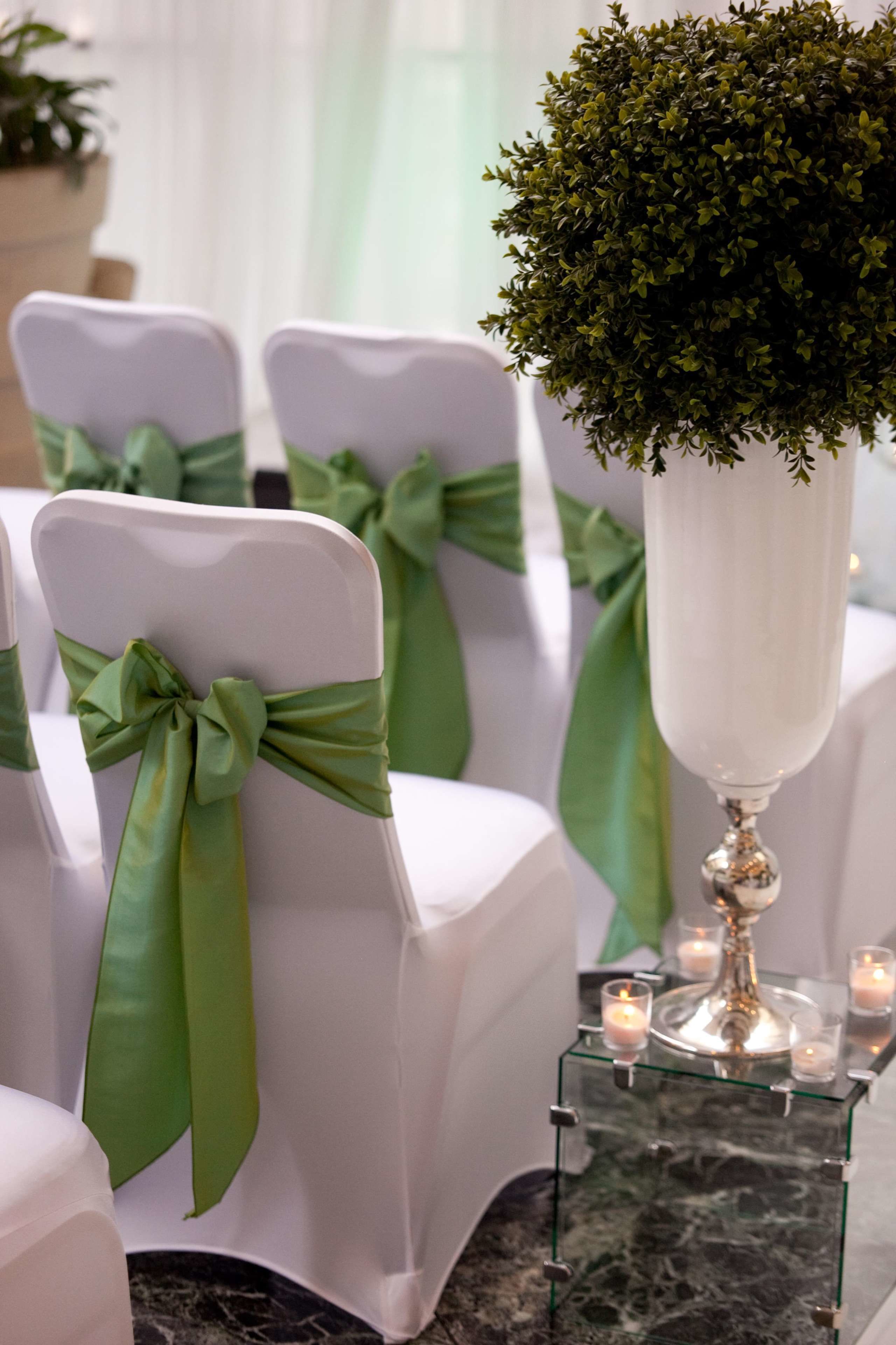 Chairs with green sashes, a glass table with candles, and a potted plant.