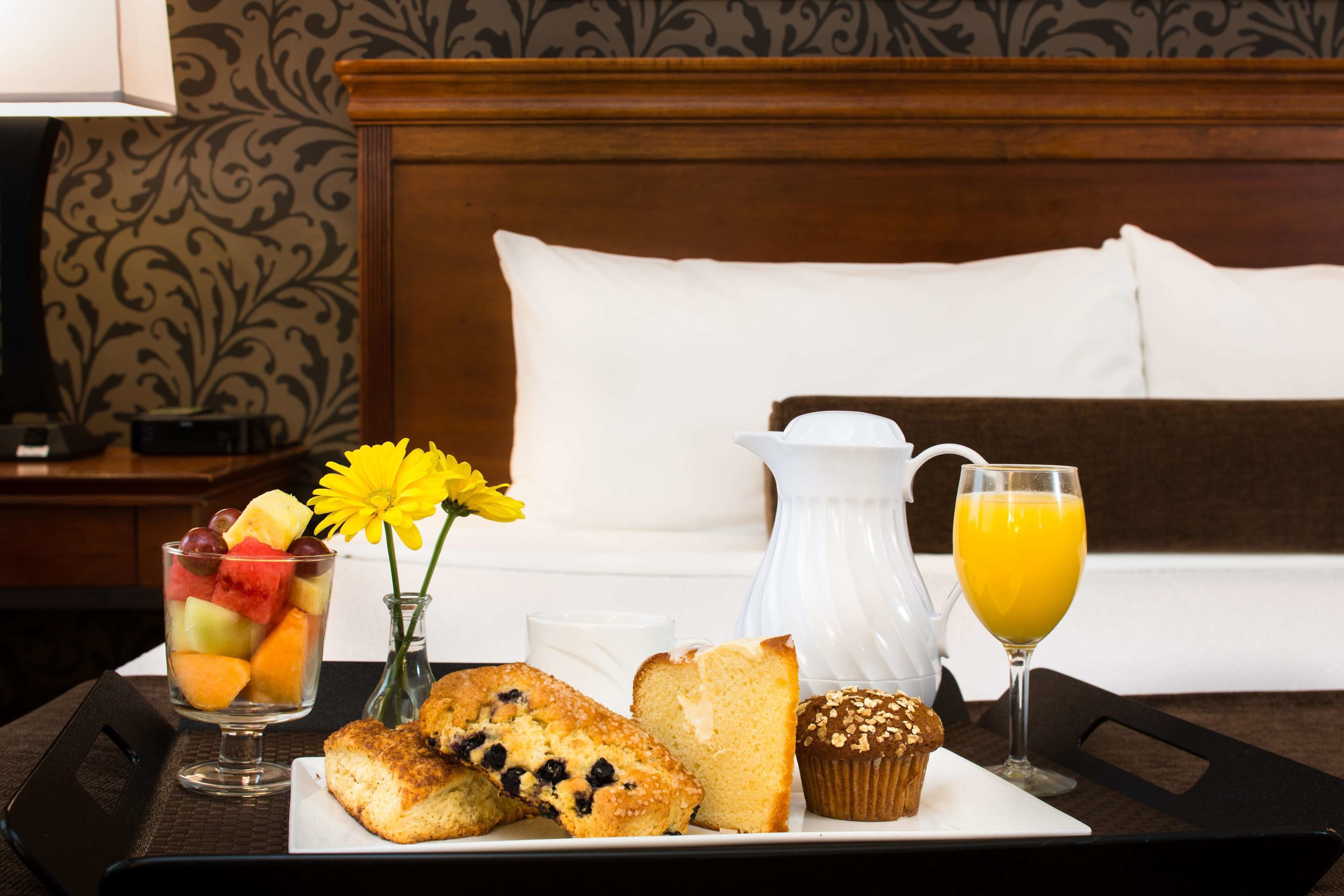 Bandeja de desayuno con fruta, muffins y jugo sobre una cama con cabecera.