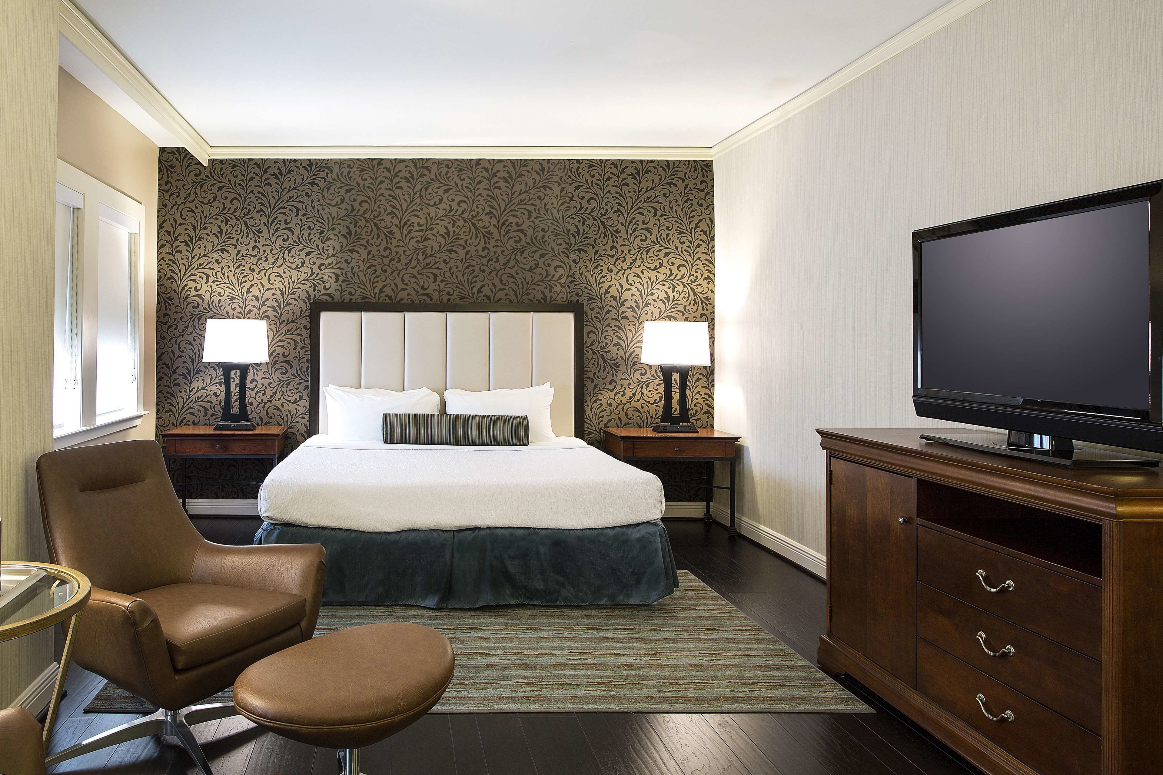 A hotel room with a large bed, a television on a wooden cabinet, a chair, and two bedside tables with lamps.