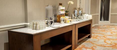 A hotel reception area with a long wooden counter, glassware, and a coffee station.