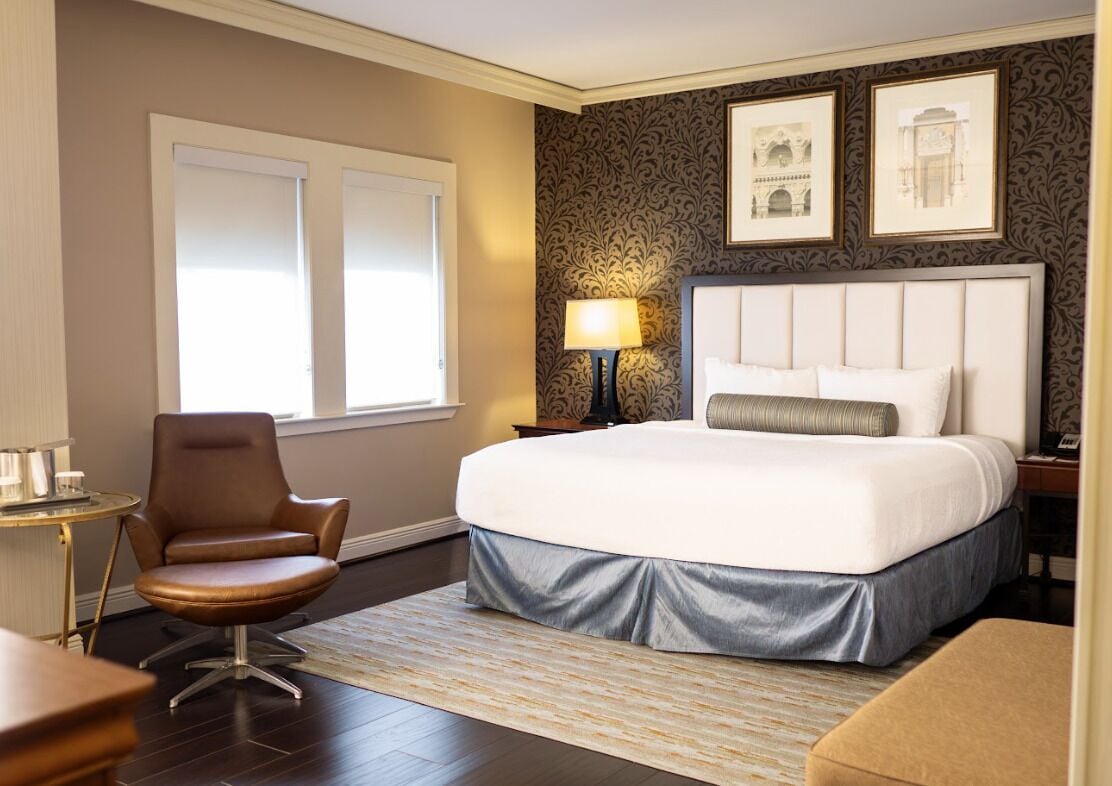 A hotel room with a large bed, a chair, a lamp, and framed pictures on the wall.