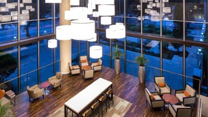 Uma sala de estar ampla com uma mesa comprida e várias cadeiras, grandes janelas com vista para a rua e iluminação pendente moderna.