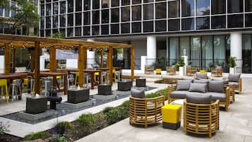 An outdoor seating area with tables and chairs, a wooden pergola, and a sign indicating a food and beverage service.