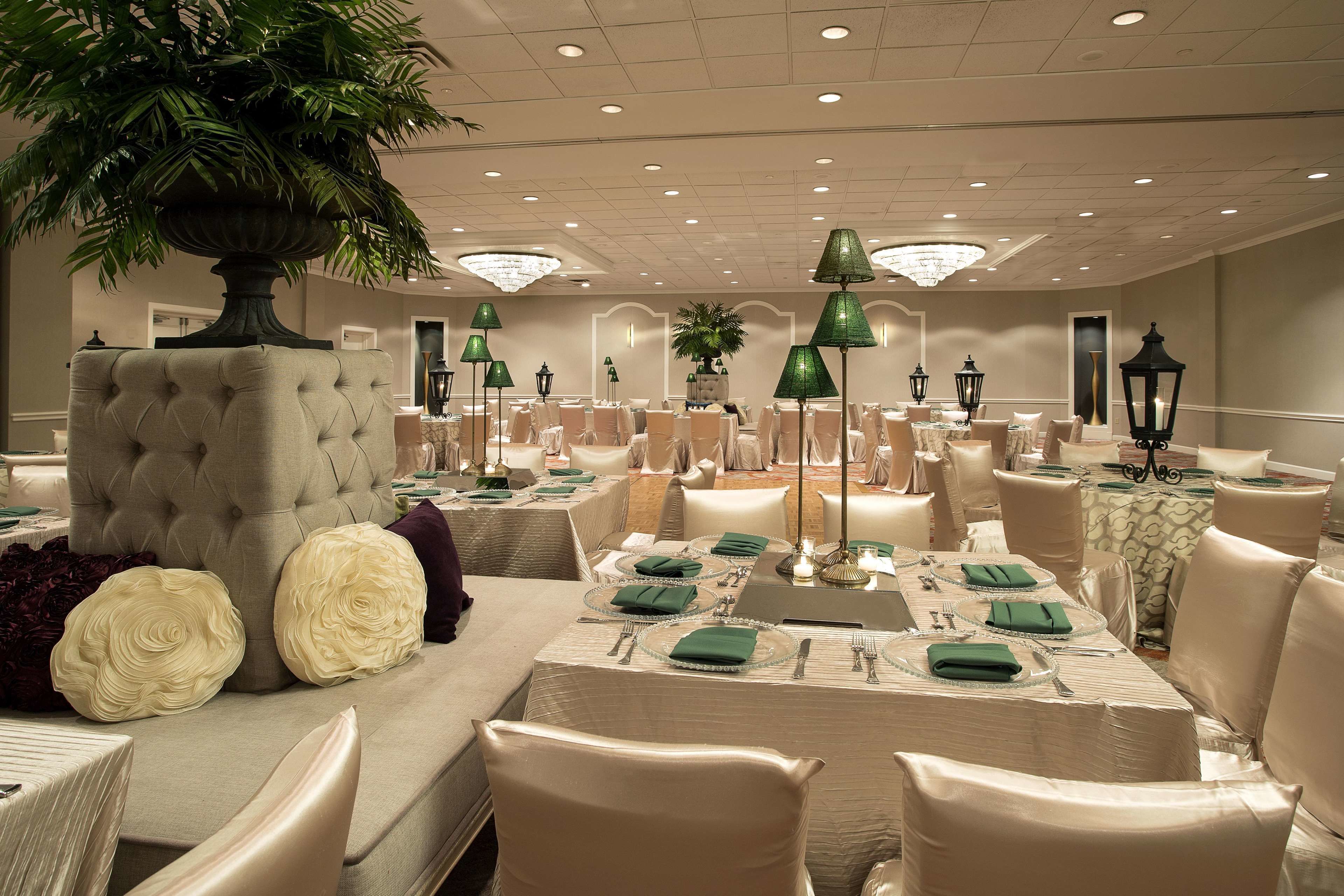 A banquet hall with multiple tables set for dining, featuring green napkins and white tablecloths.