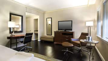 Habitación de hotel con cama, escritorio, silla, televisor y una mesita de noche con lámpara.