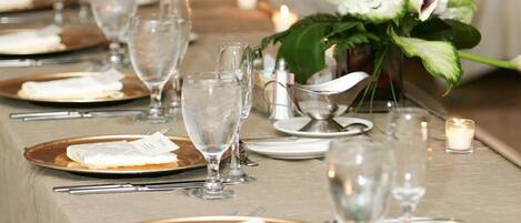Uma mesa de banquete posta com pratos, copos e velas, indicando uma disposição formal para refeições.