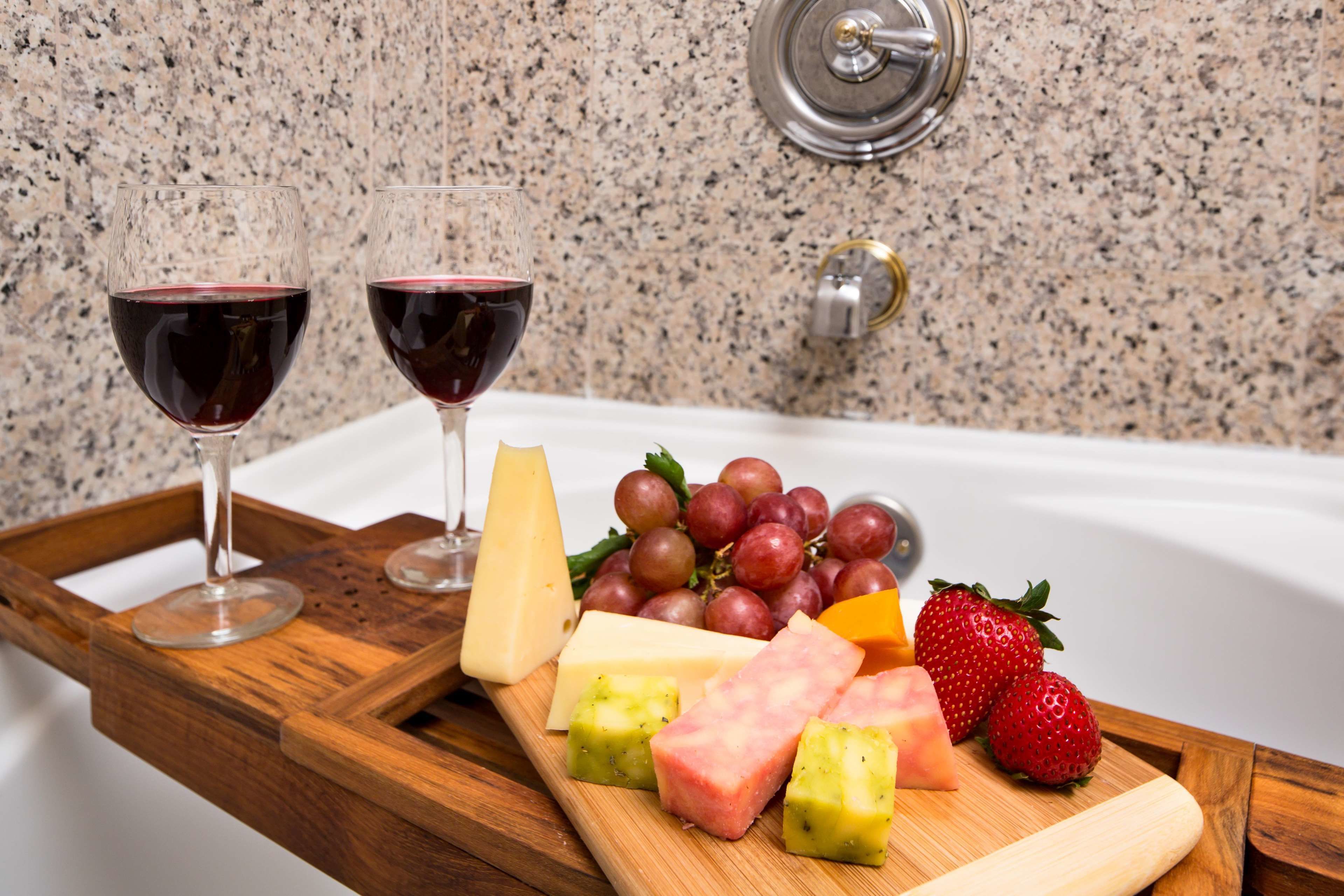 A wooden tray with wine glasses, cheese, grapes, strawberries, and watermelon slices on a countertop.