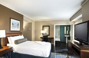 Quarto de hotel com uma cama grande, uma escrivaninha, uma televisão e um banheiro com pia e espelho.