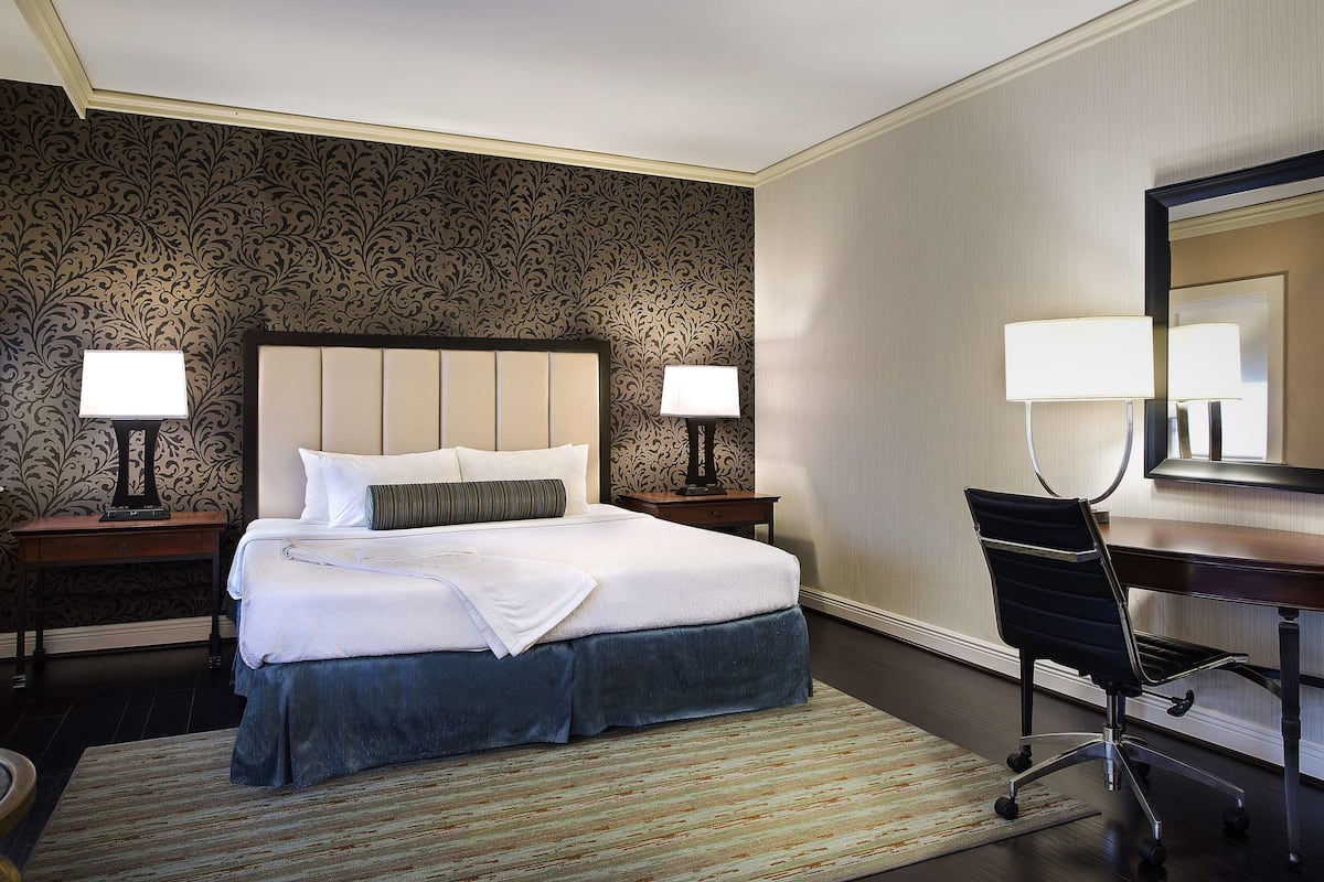 Ein Hotelzimmer mit einem Bett, zwei Nachttischen mit Lampen, einem Schreibtisch mit Stuhl und einem großen Spiegel.