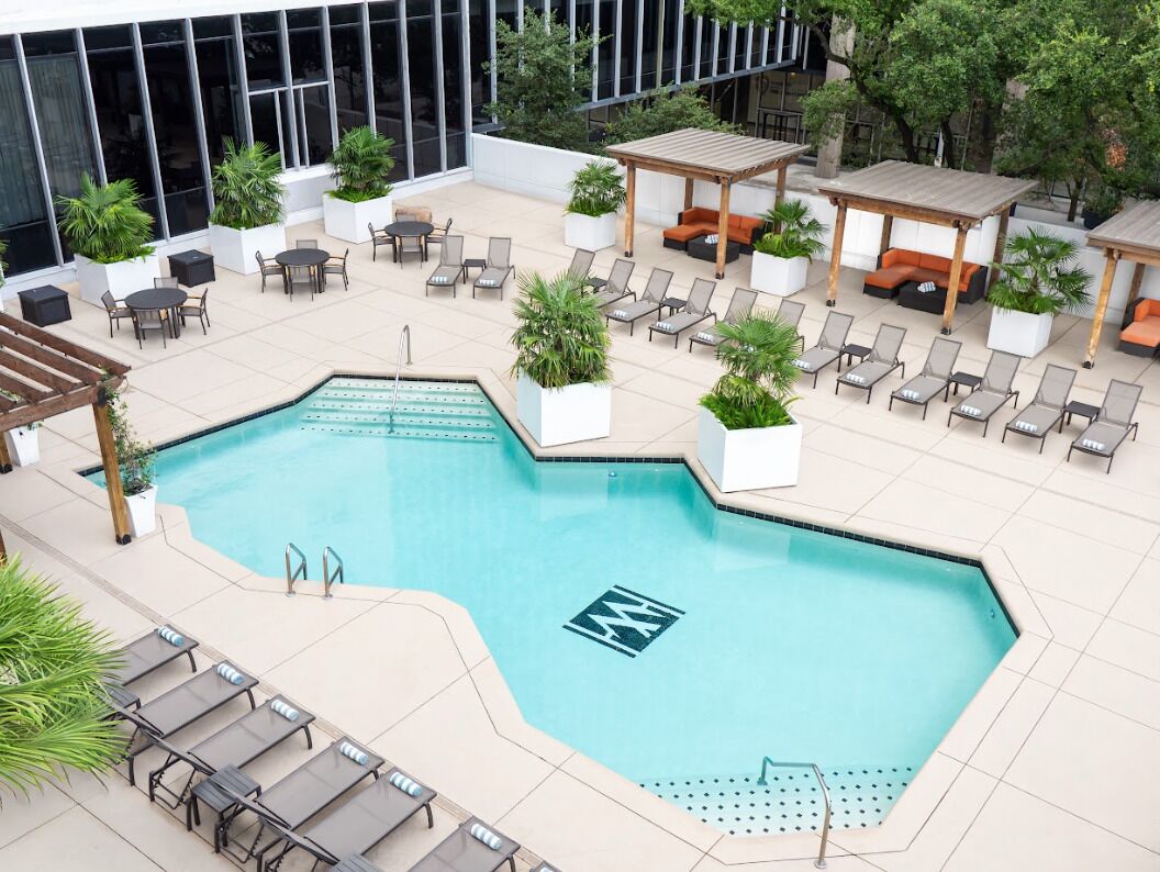 A rooftop pool area with lounge chairs, a wooden pergola, and potted plants.