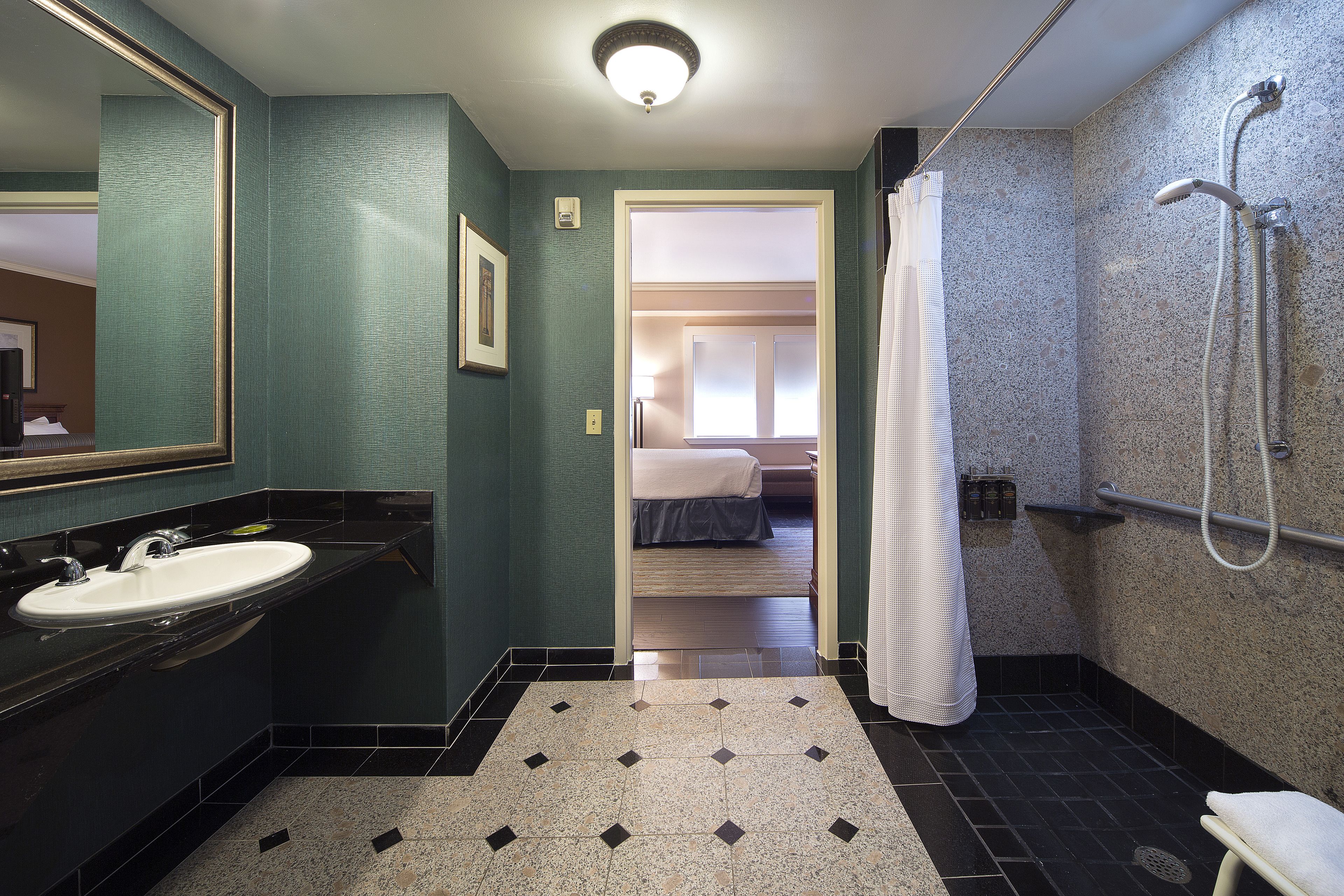 A bathroom with a sink, mirror, shower, and a door leading to a bedroom.